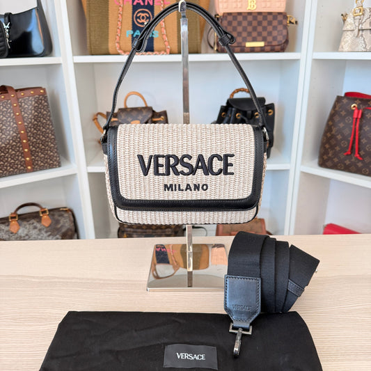 Versace handbag displayed on a stand with a shelf of other handbags in the background.
