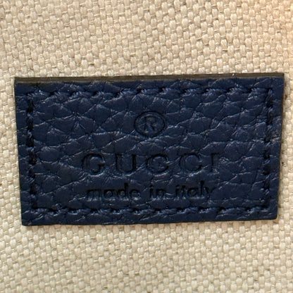 Luxe Vault blue embossed leather Gucci brand tag with Made in Italy stamp on a textured fabric background