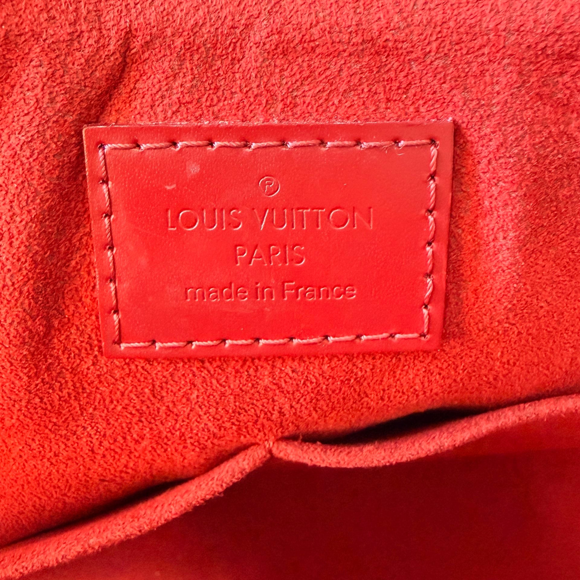 Luxe Vault interior view of a red Louis Vuitton Caissa PM bag featuring the embossed leather brand logo patch