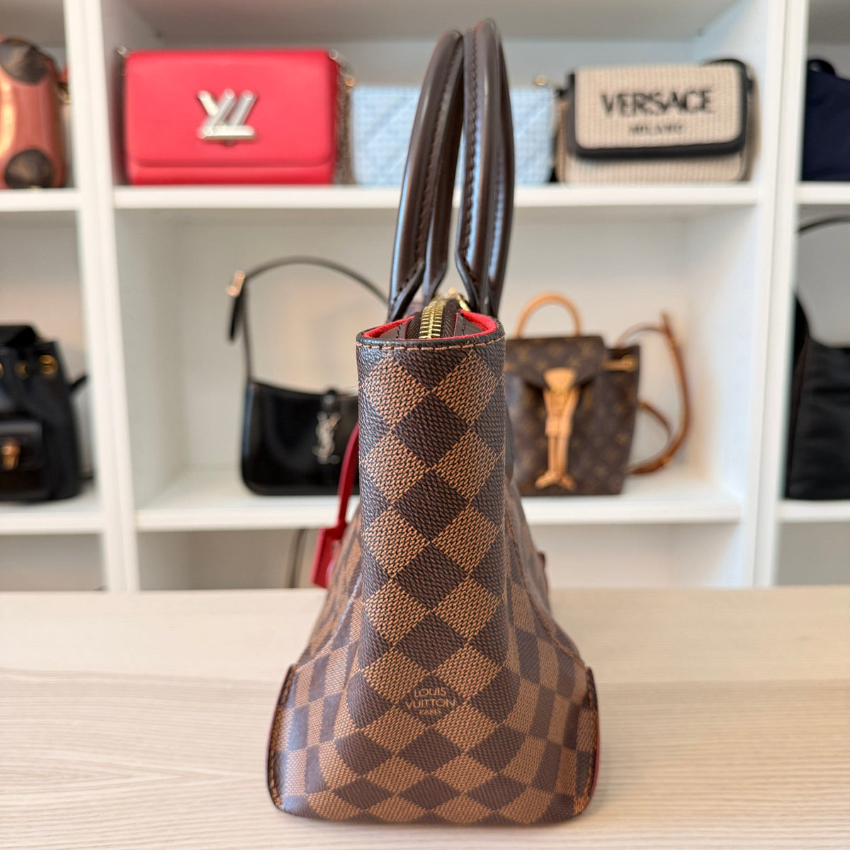 Side view of a pre-owned Louis Vuitton Caissa PM handbag in Damier Ebene canvas with brown leather handles